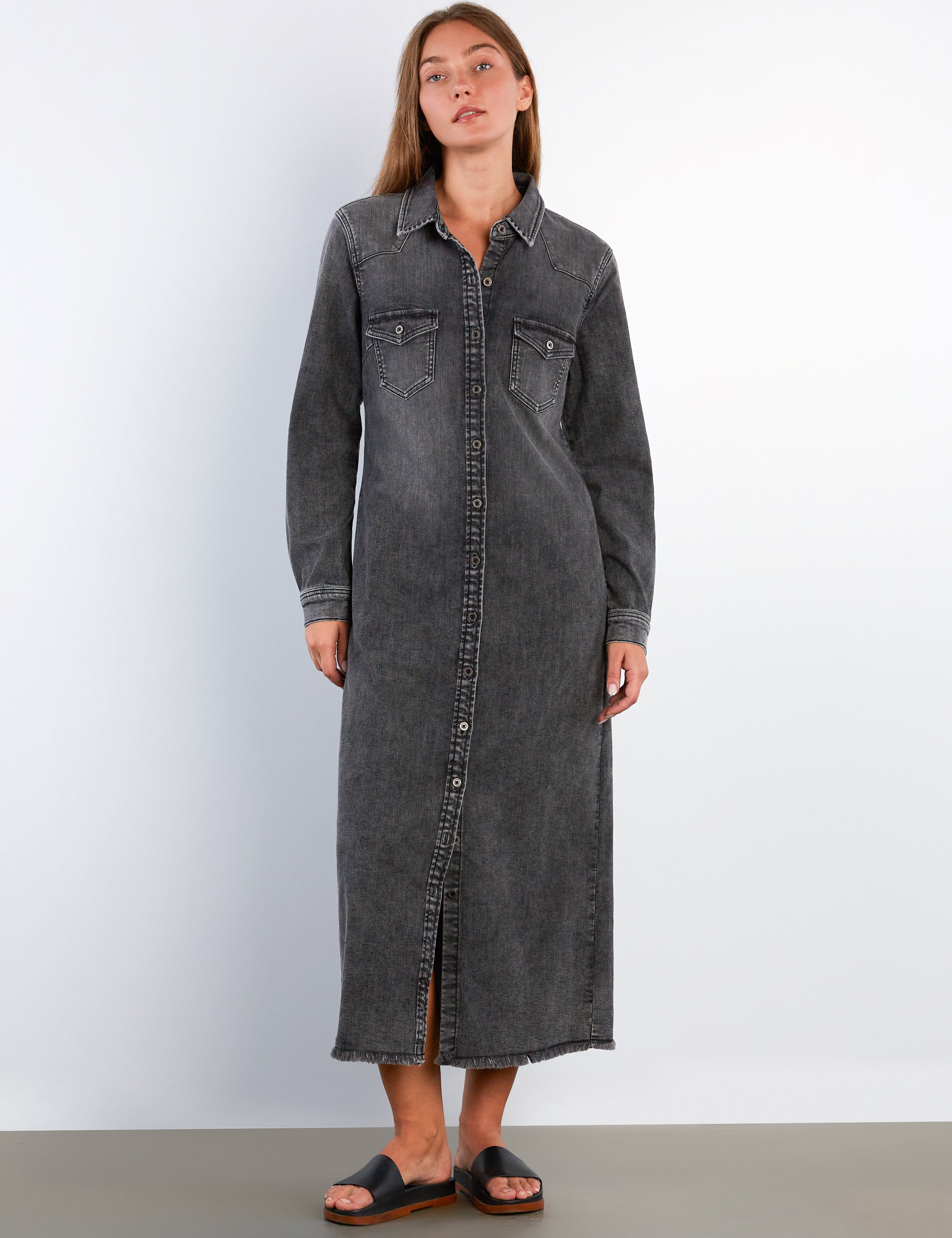 Woman wearing a long black denim dress against a white background